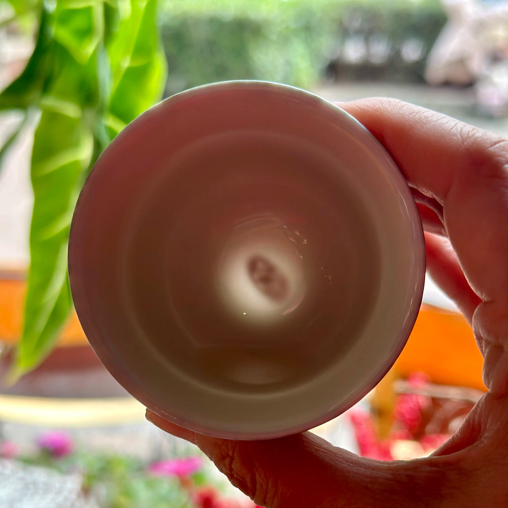 Glazara porcelain teacup held against the light, revealing the hidden artisan's signature at the base through the translucent clay body.