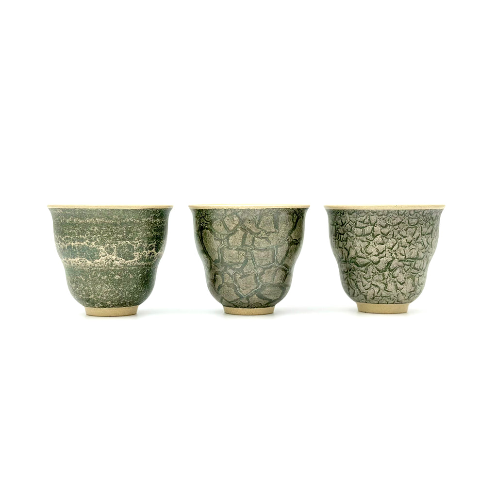 Front view portrait of three 50ml Glazara Verdant Orchid teacups standing side by side, comparing the unique hand-painted Moss Dust, Shattered Ice, and Glacier Crackle green glaze patterns.