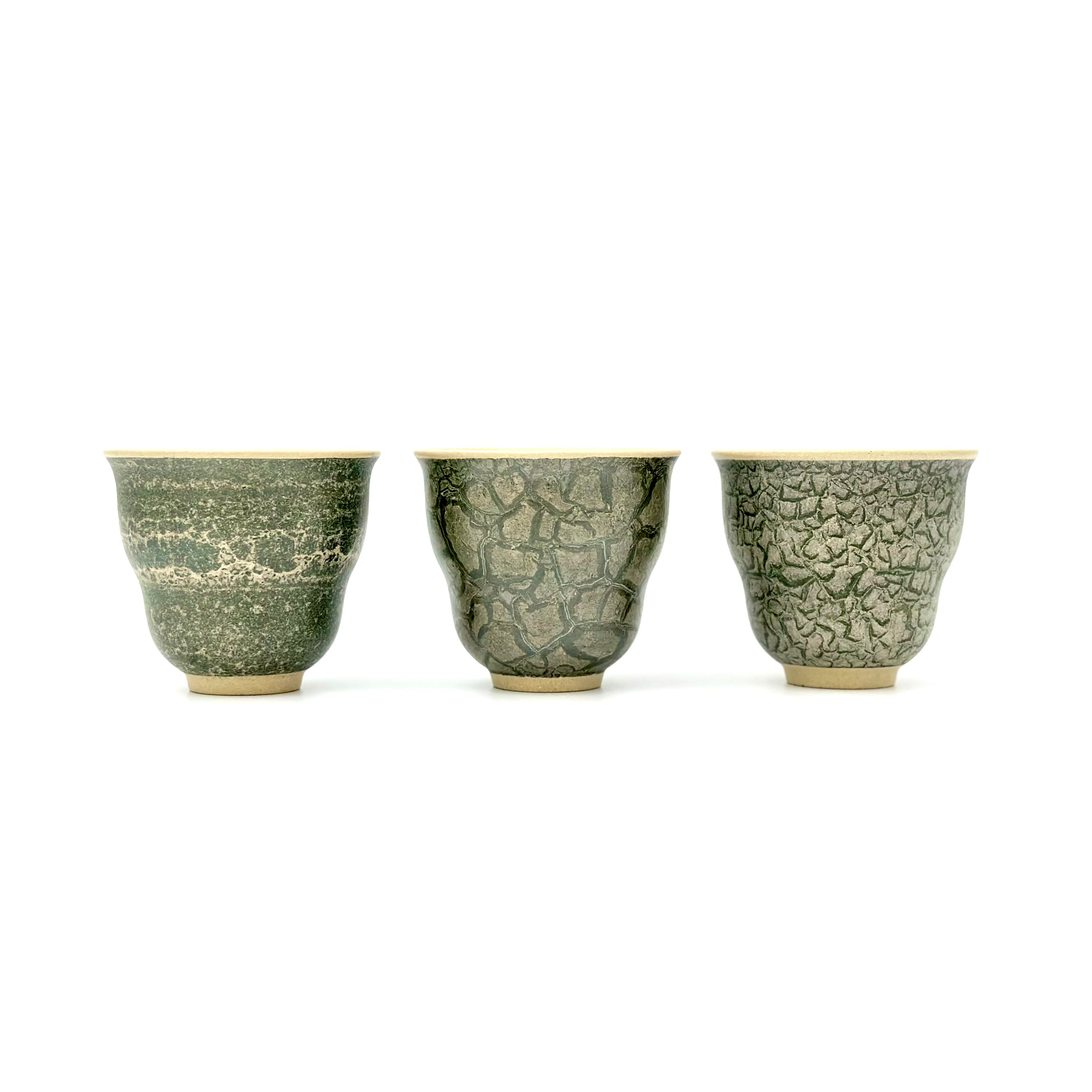 Front view portrait of three 50ml Glazara Verdant Orchid teacups standing side by side, comparing the unique hand-painted Moss Dust, Shattered Ice, and Glacier Crackle green glaze patterns.