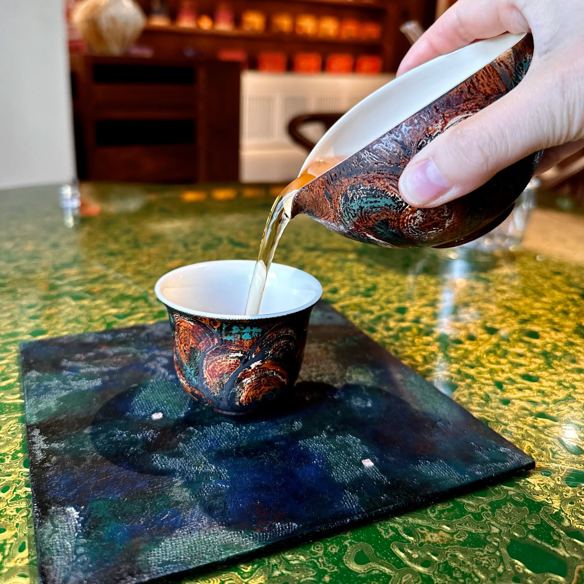 Lifestyle view of pouring specialty tea from the 120ml Glazara Vintage Flora lacquer tea pitcher, a modern porcelain Gongdao Bei designed for Gongfu tea rituals.