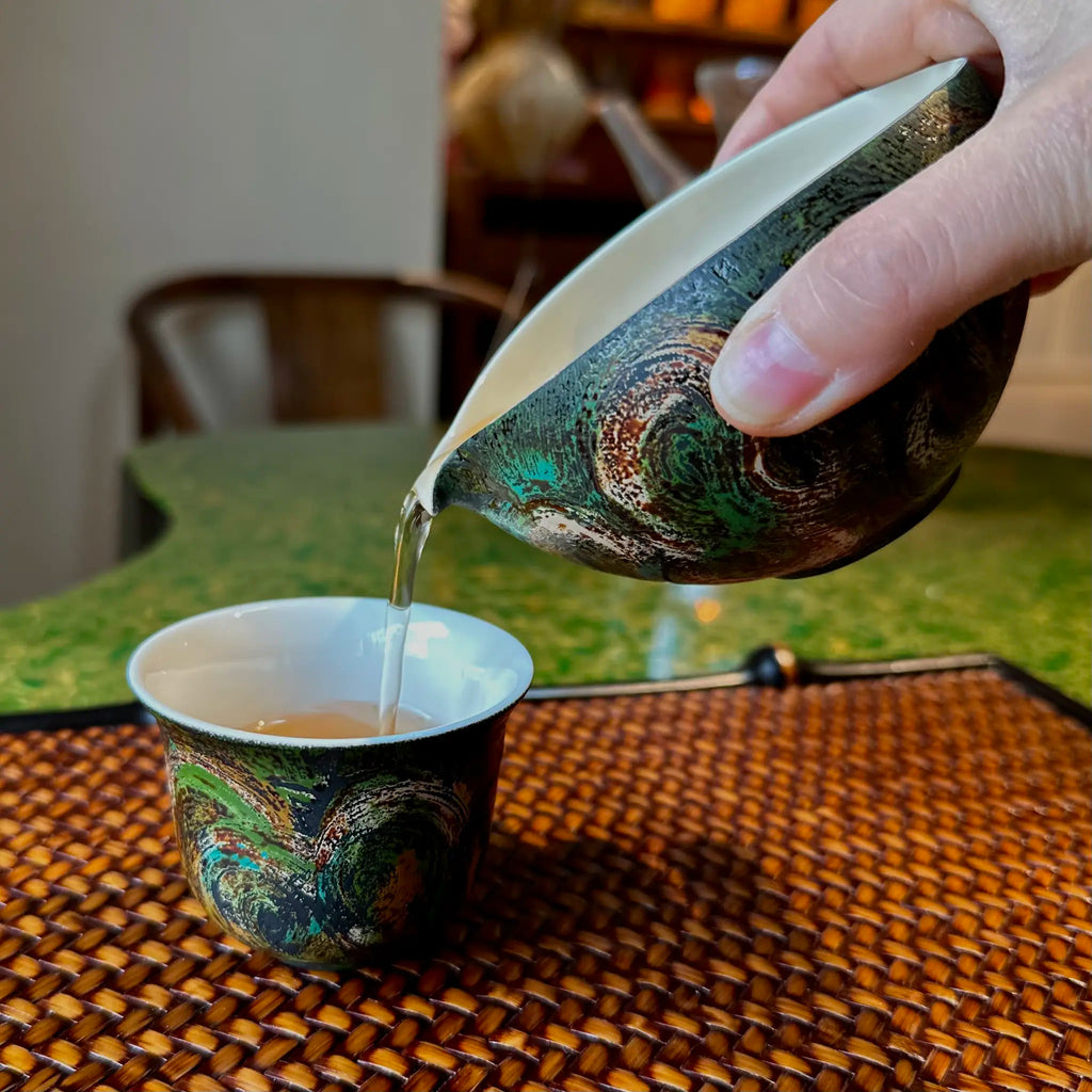 Lifestyle view of pouring tea from the 120ml Glazara Viridian Twilight urushi tea pitcher, a modern porcelain Gongdao Bei designed for Gongfu tea rituals.