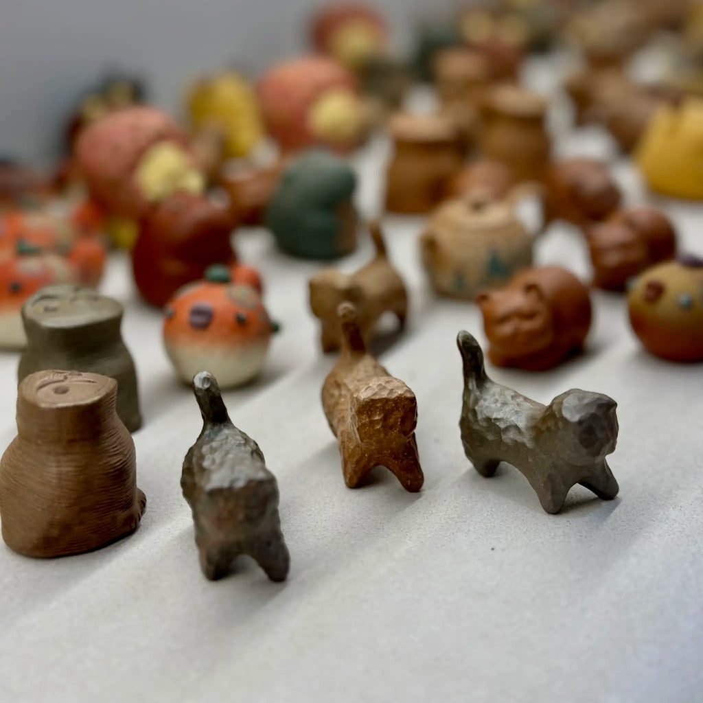 A high-angle group shot of various wood-fired Yixing clay tea pets. Three distinct cat tea pets confidently lead the group in the front row, resembling a playful, wandering gang.