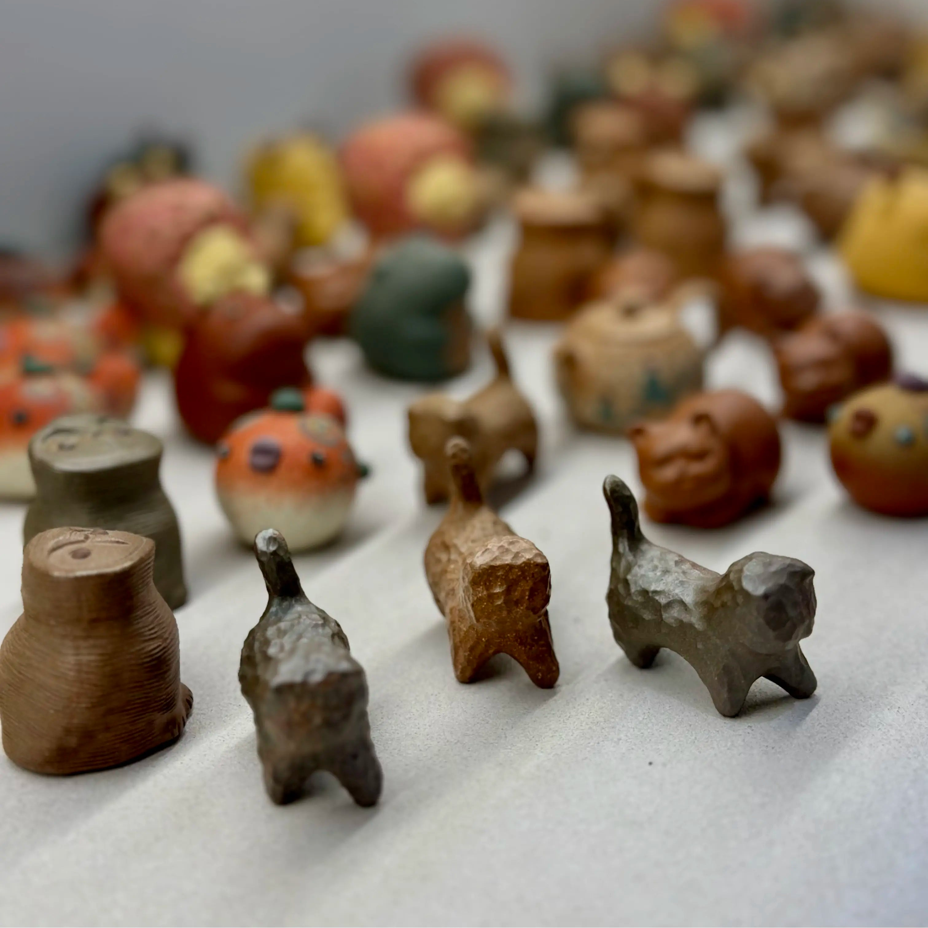 A high-angle group shot of various wood-fired Yixing clay tea pets. Three distinct cat tea pets confidently lead the group in the front row, resembling a playful, wandering gang.
