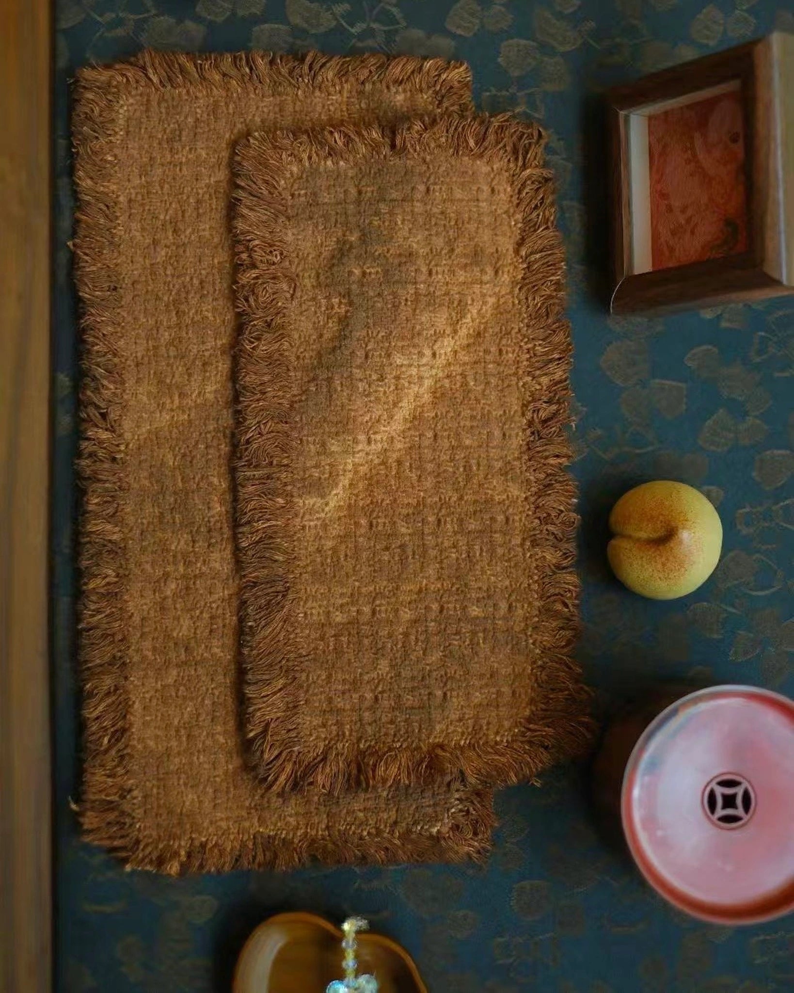 An overhead view of a traditional tea table setting featuring two layered persimmon-dyed tea mats, with the small mat resting elegantly on top of the medium mat, ready for a tea ritual.