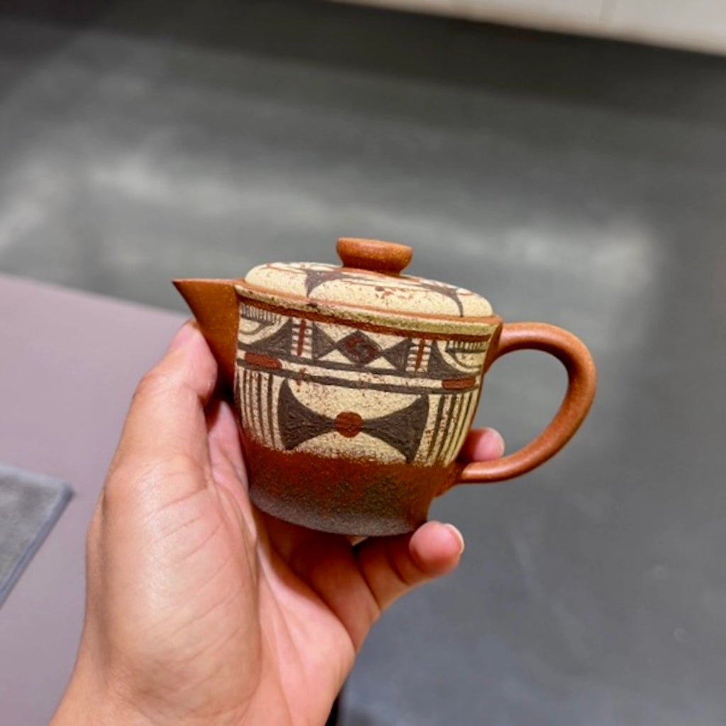 Close-up of a hand holding the Neolithic Echo Yixing teapot's handle, featuring the fluid, 7,000-year-old Yangshao-inspired hand-painted motifs.