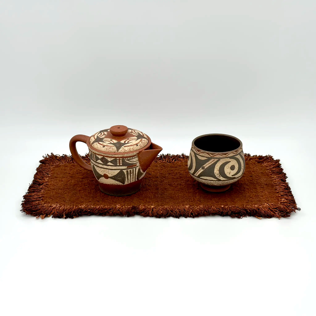 Studio shot of the Neolithic Echo painted Yixing Zisha teapot alongside a matching classic painted teacup, arranged on a traditional tea mat.