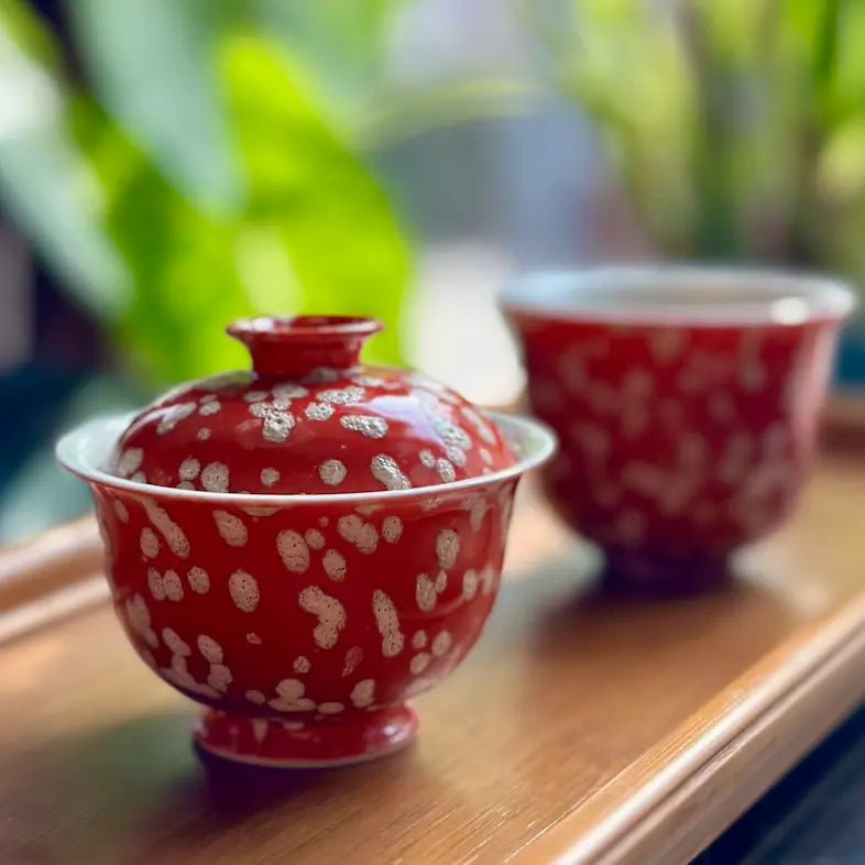 Lifestyle shot of the Phoenix Spark Solo Gaiwan and matching teacup resting on a natural bamboo tea tray. The contrast between the warm wood and the vibrant, fiery red glaze creates a serene and grounded atmosphere for tea tasting.