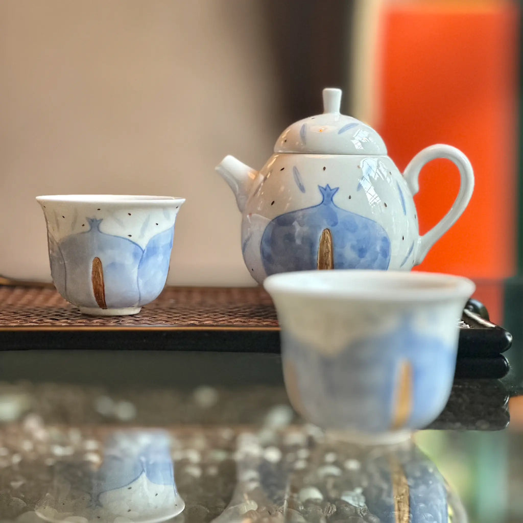 Ceramic teapot and cups with blue and white design on a reflective surface.